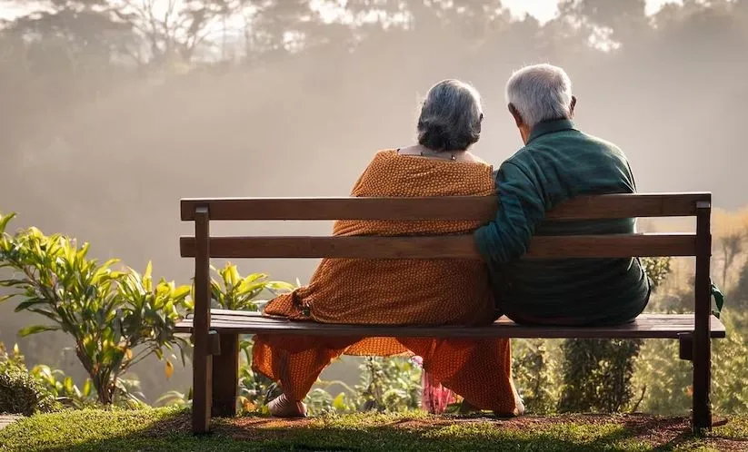 Una pareja de adultos mayores sentados juntos en una banca de madera en un parque